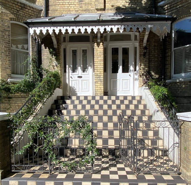 A symmetrical entrance to a Victorian-style terraced house in Hoxton with a staircase leading up to a white door, flanked by small garden beds with green shrubs and plants. The staircase is paved with